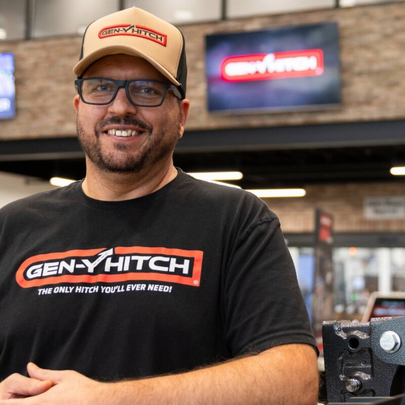 Man wearing GEN-Y HITCH branded shirt and cap standing in automotive showroom