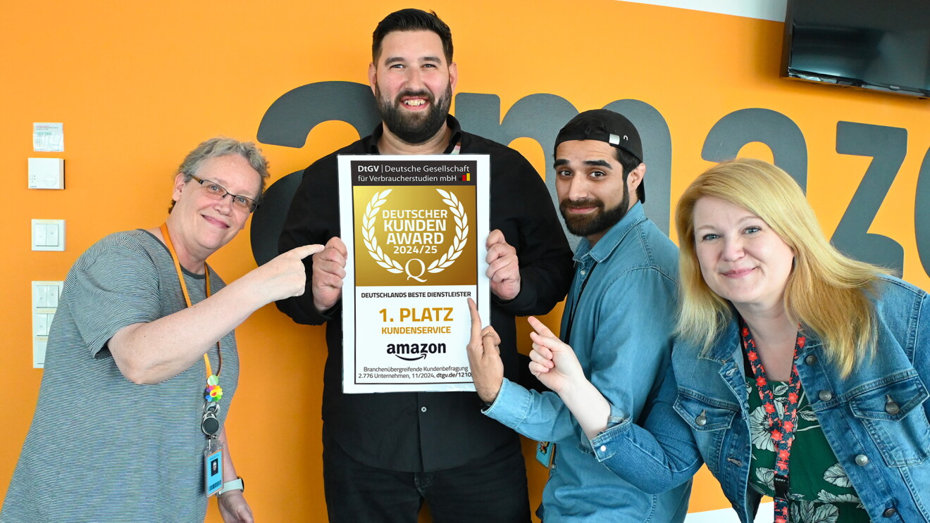 4 Mitarbeiterinnen und Mitarbeiter aus dem Amazon Kundenservice halten ein ca. DIN A3 großes Siegel hoch auf dem zu lesen ist: "Deutscher Kundenservice Award 2024/25, 1. Platz Kundenservice Amazon".