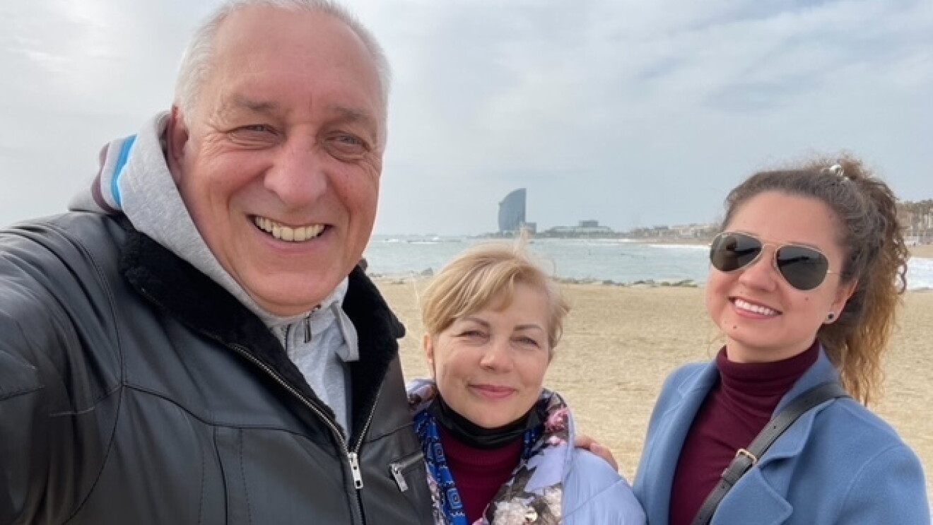 Daria and parents smile for a picture on a beach in Spain.