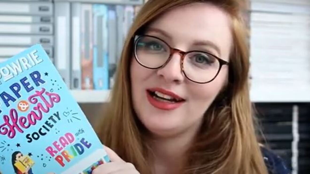 Girl holding a book up and smiling at camera 