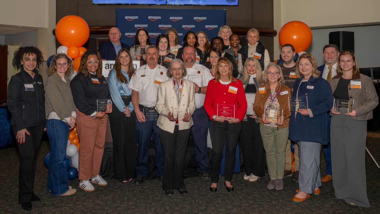 Large group poses with awards at Amazon event with orange and blue balloons