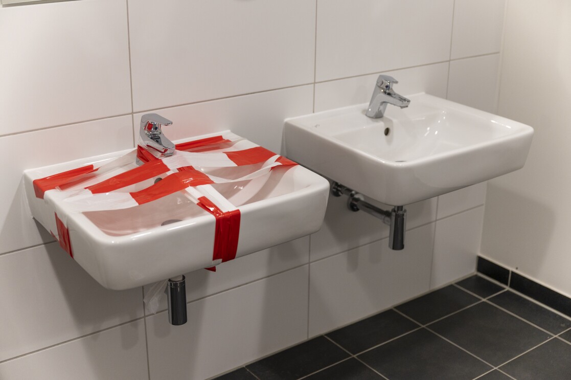 2 Waschbecken in einem Sanitärraum: eines davon ist mit Sicherheitsbändern umwickelt und nicht für die Benutzung gedacht, um die Sicherheitsabstände zu gewährleisten.