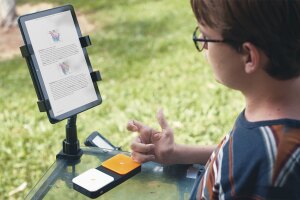 Teenager in a motorized wheelchair using a Bluetooth switch button connected to his Fire tablet to read a book.