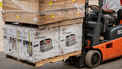 A man working with Amazon's disaster relief team is driving a forklift loaded with generators at the front. These generators will be used to provide power to those affected by recent natural disasters in the U.S.
