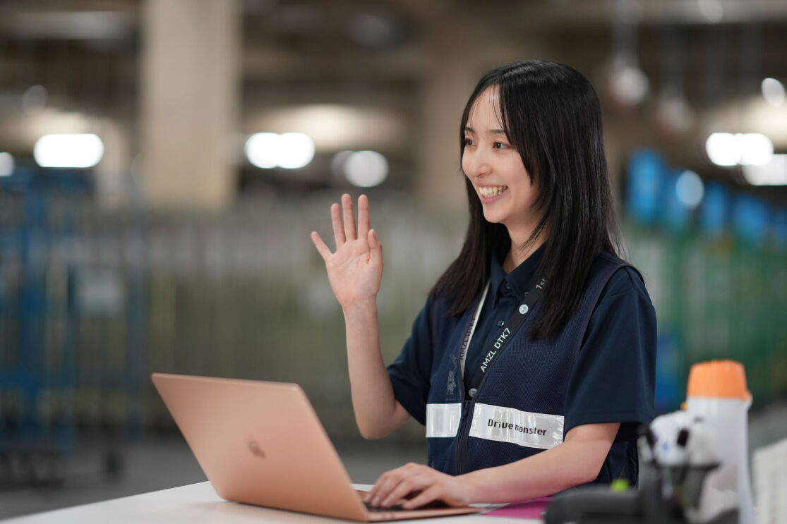 広い空間の中に座っている女性がパソコンを操作しながら手を振っている。