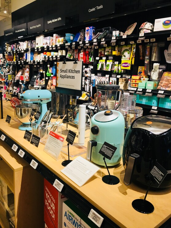 A display area in Amazon 4-star. A display area of Small Kitchen Appliances has a KitchenAid Mixer, Sous Vide, air fryer, food processor and more. Behind the display are sections for "Cooks' Tools," "Kitchen Gifts," "Bar and Party Supplies," "Quirkly Kitchen Gifts," and more.