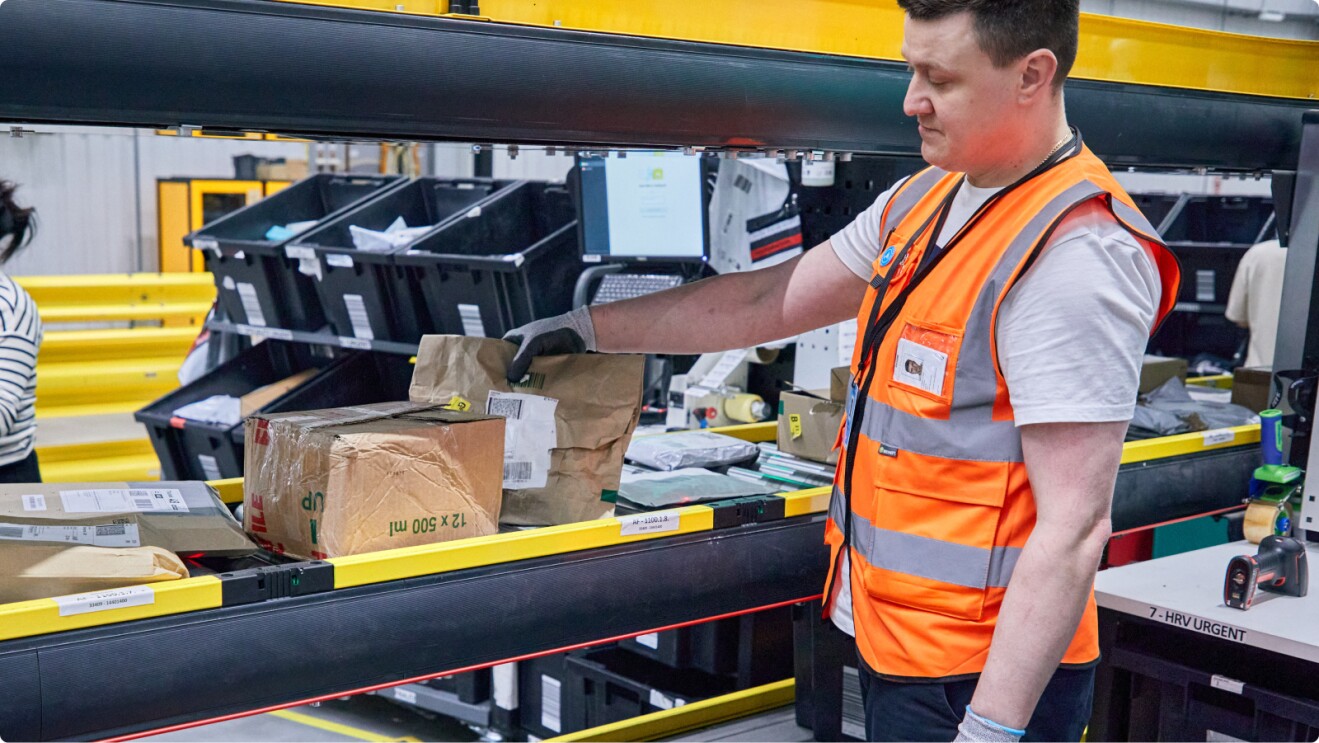 Amazon associate retrieving returned parcel from conveyor belt