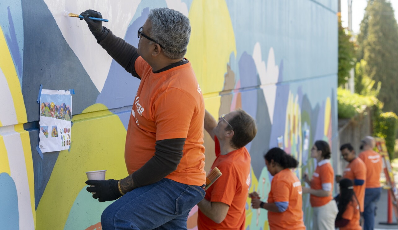 A group of Amazon volunteers work on a colorful student-designed mural at Emerson Elementary