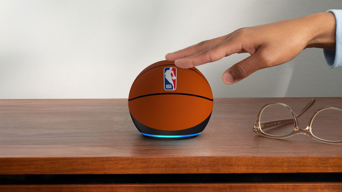 木製の家具の上に置かれた球状の小さなデバイスに、人の手が触れている。デバイスはバスケットボールを模したデザイン。