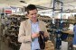 José Antonio Mollá, fundador de Castellanisimos, en una de sus fábricas, observando un zapato castellano que tiene en sus mannos. Detrás hay cahas de zapatos y una persona trabajando en una mesa. 