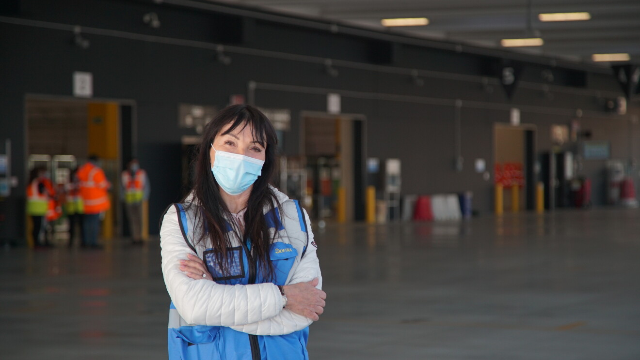 Foto di una dipendente di Amazon in un magazzino. Indossa un giubbino di sicurezza azzurro, ha le braccia conserte 