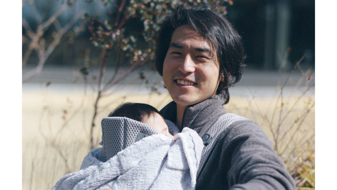 抱っこ紐でお子さんを抱く笑顔の田中さんの写真