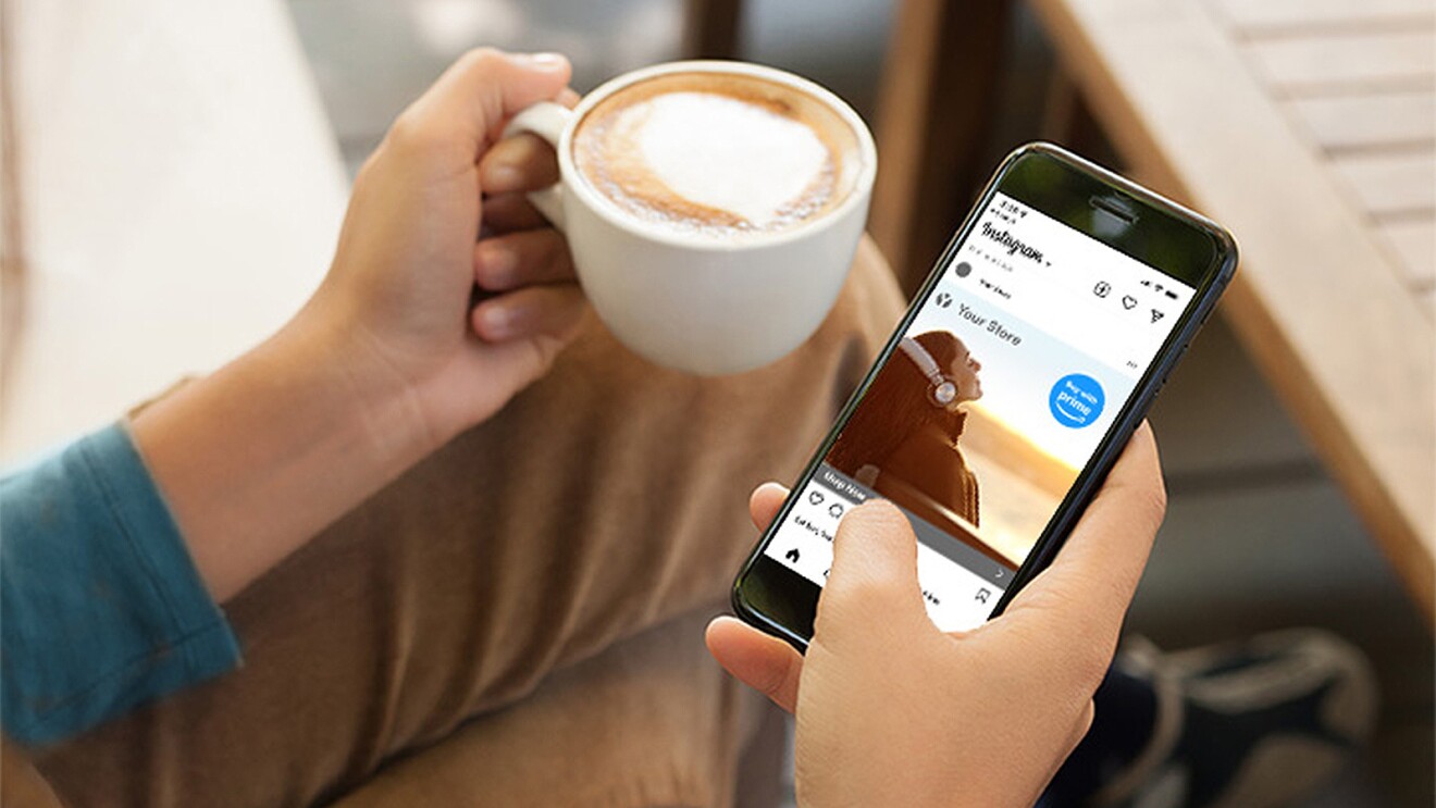 An image of a person's phone showing Instagram, being held with one hand, and the other hand holds a mug with coffee.