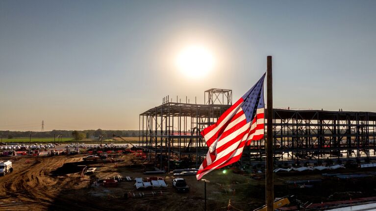 American flag waves over construction site of new building at sunset