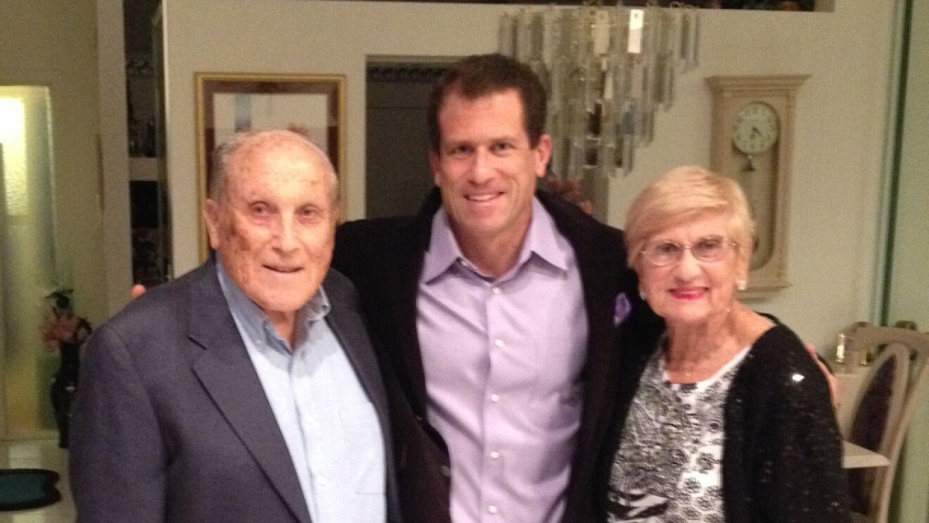 An image of an adult son standing between his mother and father in their home.
