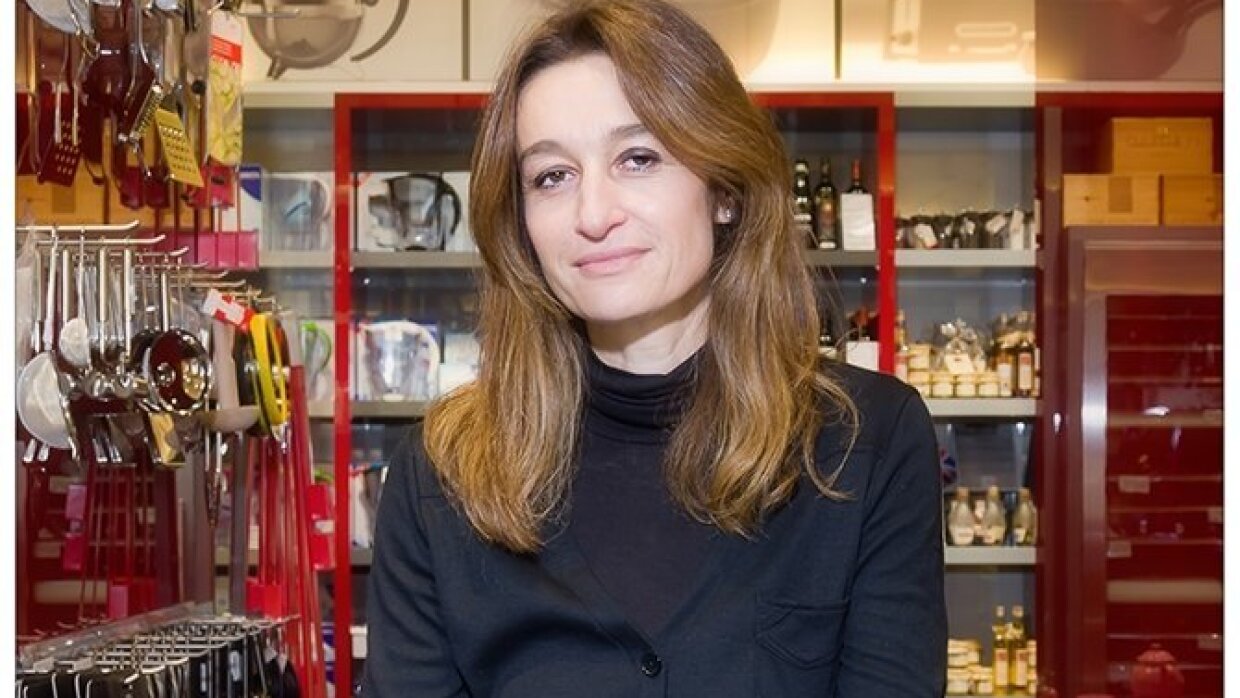 Valérie Le Guern Gilbert se tient devant des vitrines et des présentoirs où sont rangés des ustensiles de cuisine : passoires, râpes, carafes...