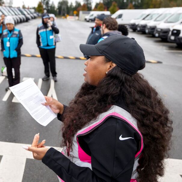 Amazon Delivery Service Partner addressing group of workers in blue vests in parking lot