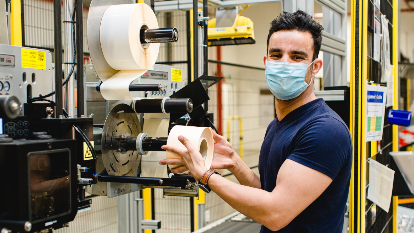 Ein junger Mann mit Maske an einer Etikettiermaschine