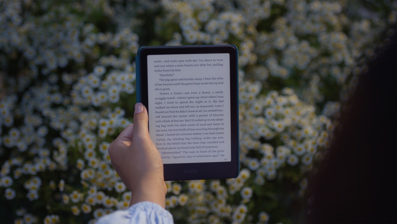 Someone holding a Kindle Paperwhite in front of a background of daisies