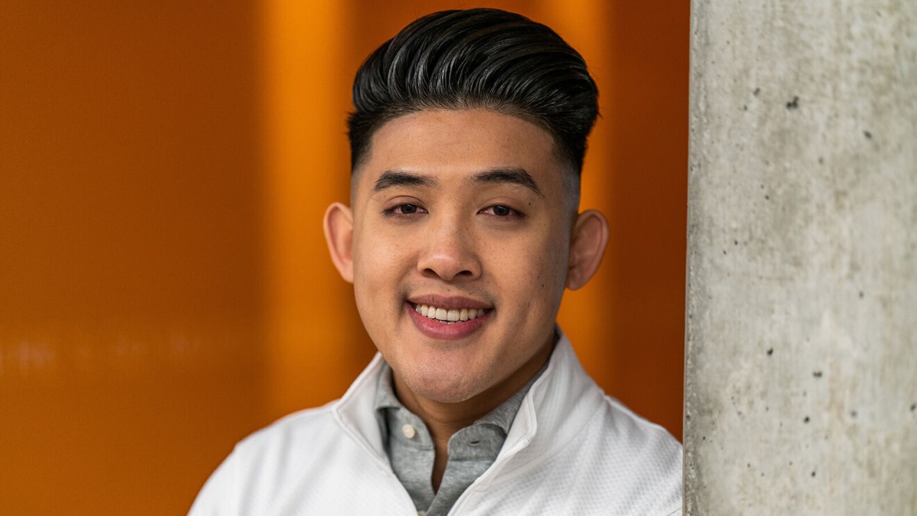 A headshot image of a man smiling for a photo in front of an orange wall.