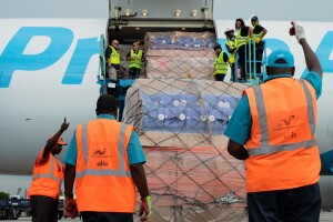 Employees in orange and yellow vests lift cargo supplies onto a Prime Air plane.