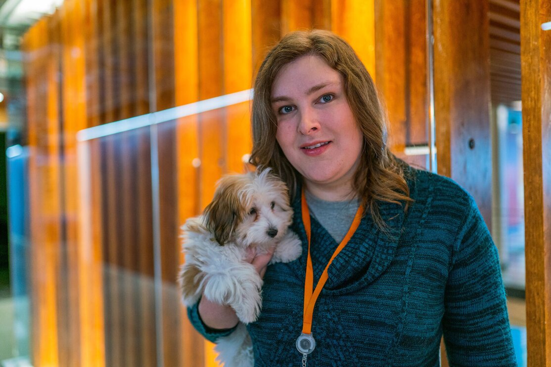 Ana Steele smiles for a photo with her small dog in front of a wood structure in Amazon's lobby.