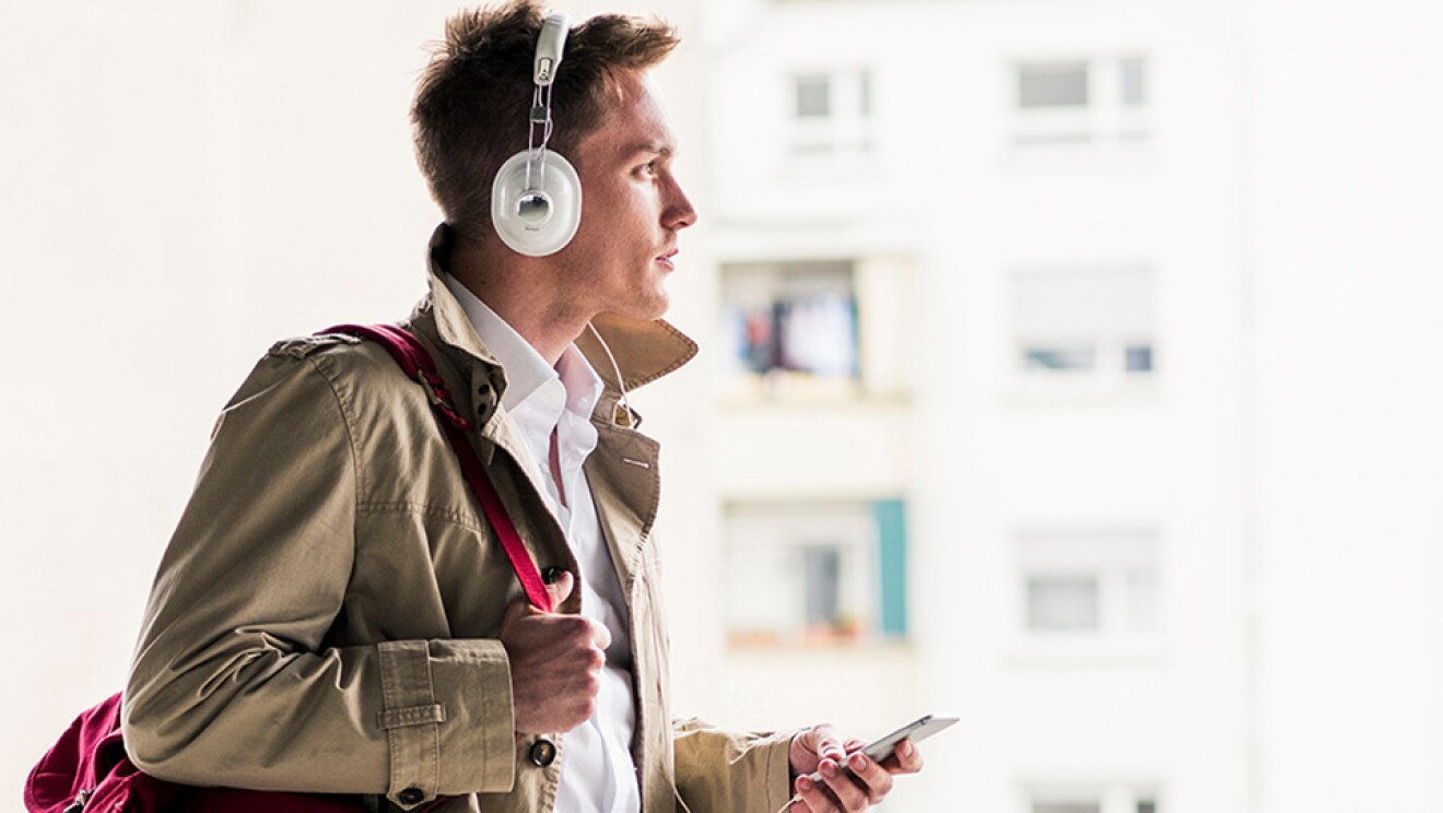 A stylishly dressed man listens to audio from his smartphone via headphones