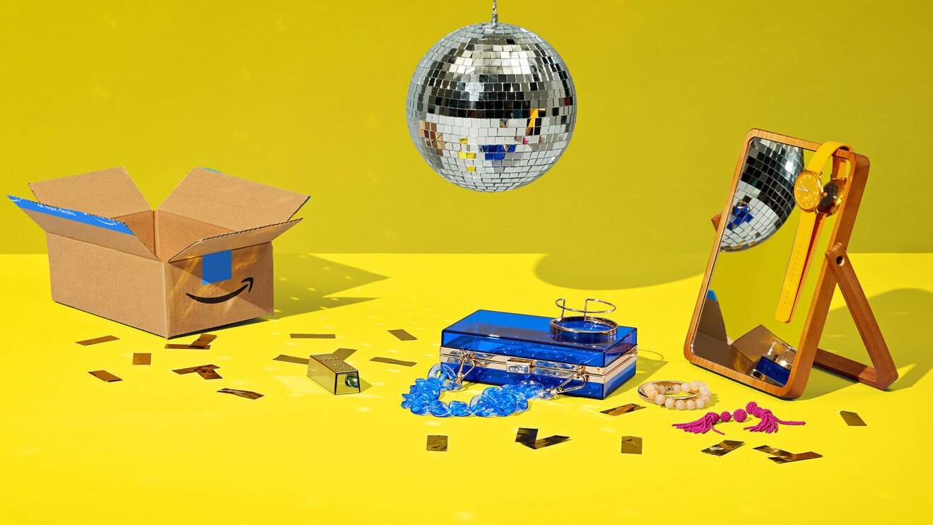 An image of disco ball floating above a display of items. There is an Amazon box, a plastic, blue purse, and a mirror with an orange watch draped on top of it. There is confetti on the ground as well as bracelets and an earring. The background for all of this is bright yellow. 