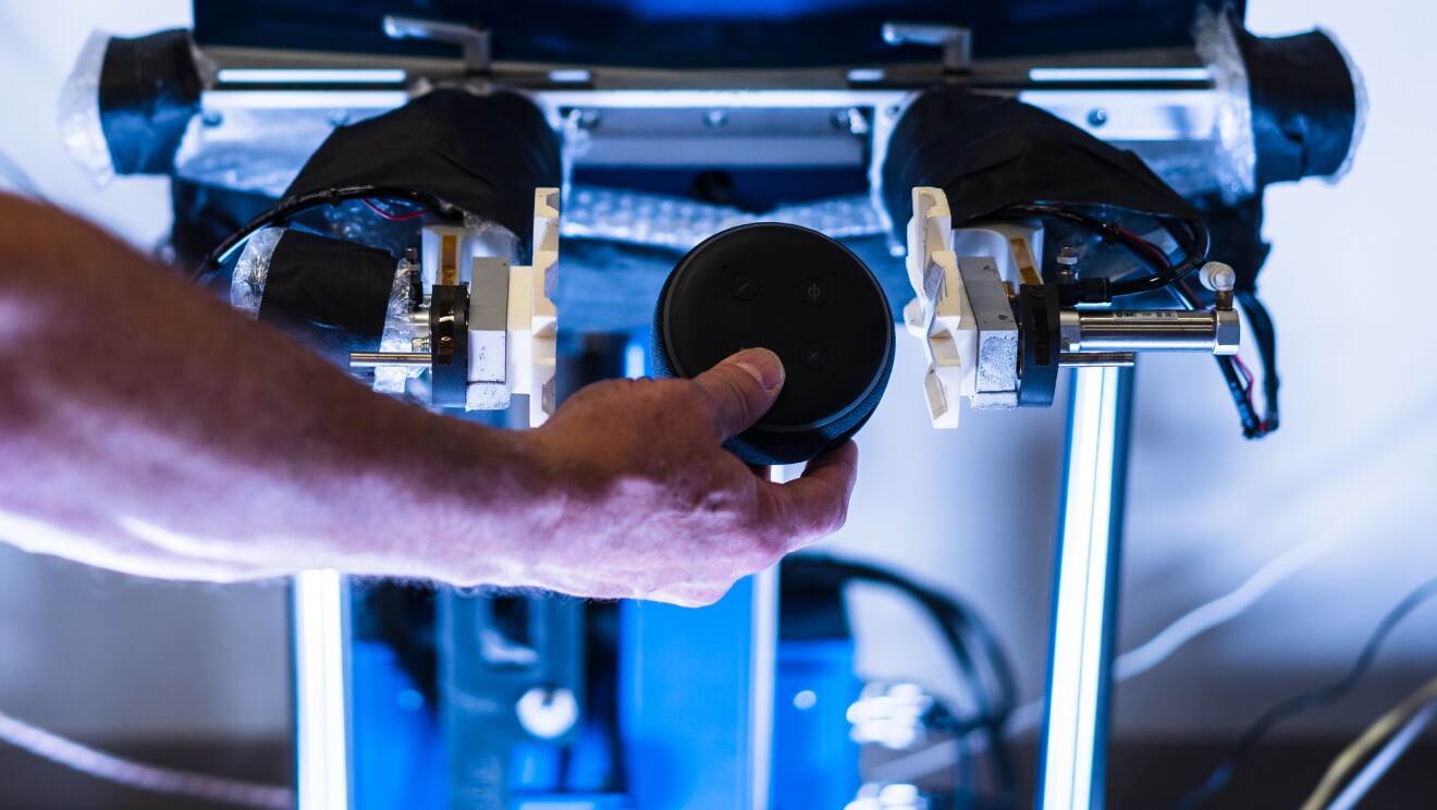 A man's arm holds a puck-shaped device near a laboratory apparatus.