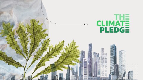 A city with tall buildings is the right backdrop of the image with The Climate Pledge in green font above it. To the left is green plant coming out from the city as tall as its buildings. To the left and behind the plant is a gray-toned drawing of the Earth.