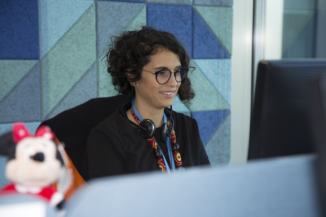 Sarah Beddini, Head of Vendor Management della sezione Giochi & Giocattoli di Amazon, siede alla sua scrivania, di fronte allo schermo del PC. In primo piano, fuori fuoco, un peluche del personaggio di Minnie. 