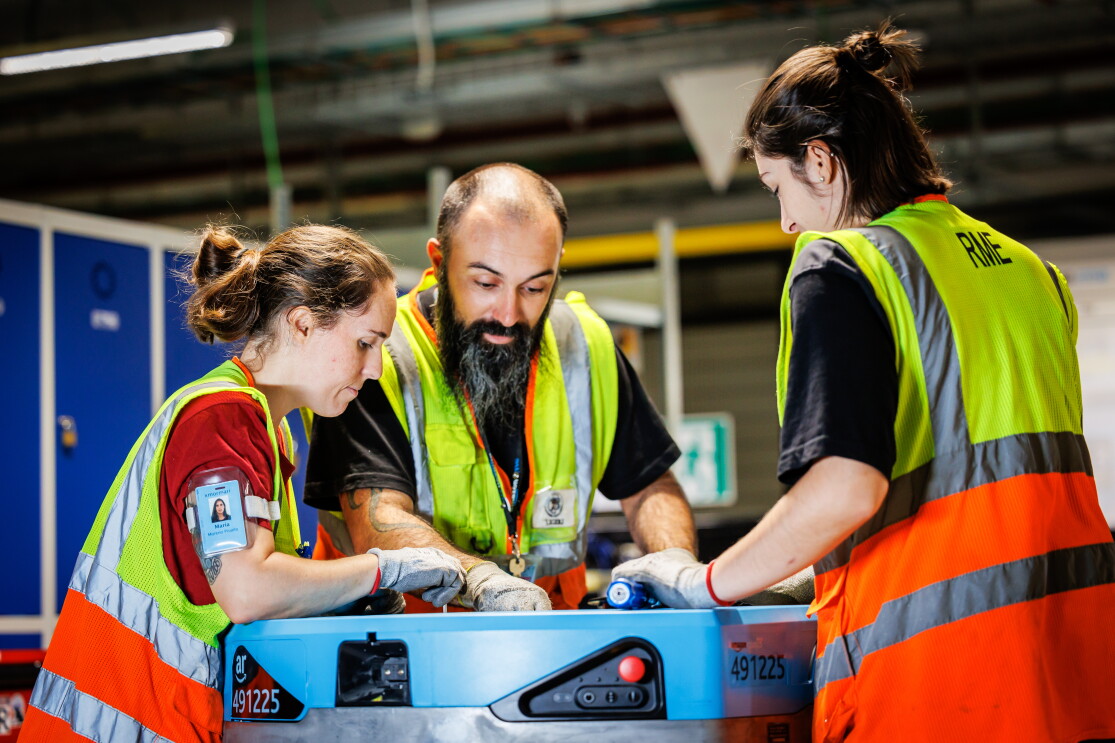 Tre trabajadores de un centro logístico de Amazon arreglando un robot. 