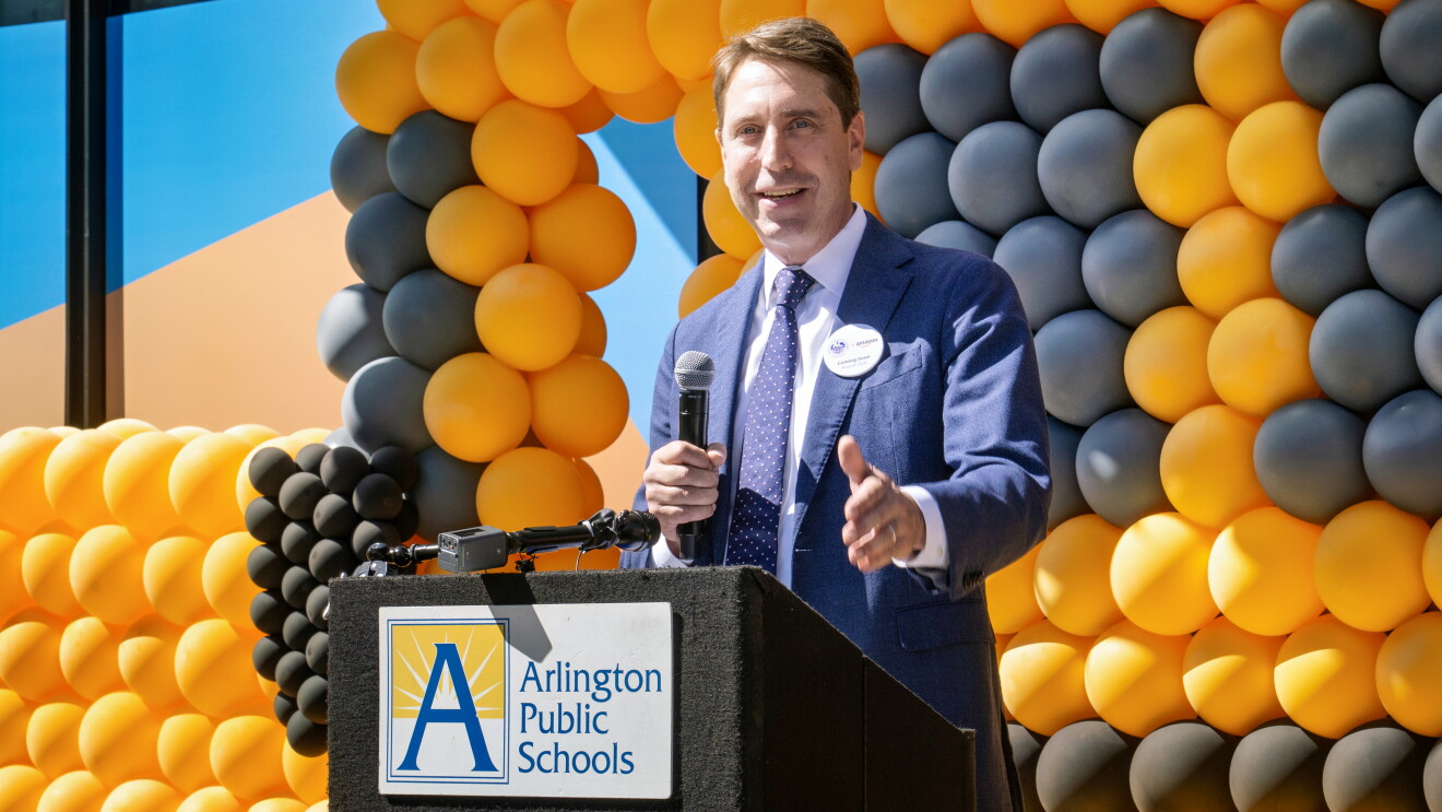 Speaker at Arlington Public Schools podium with balloon backdrop