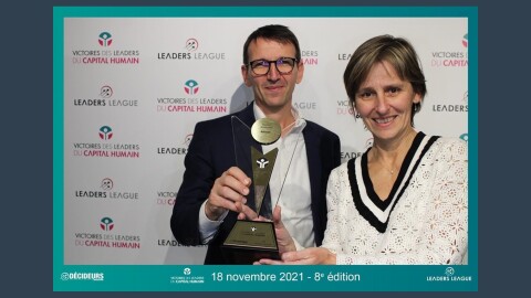 A man and a woman stand in front of a background that says "Leaders League" and "Victores des leaders du capital humain" - they hold a trophy
