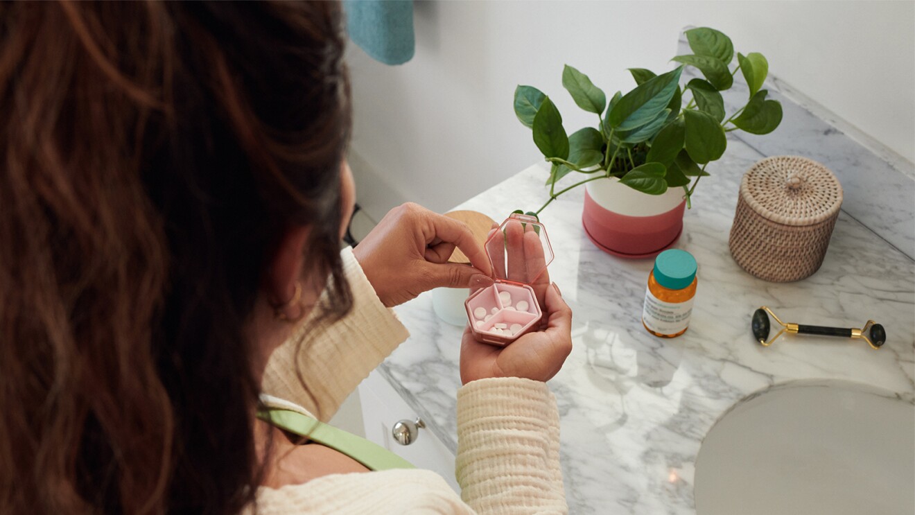 overhead view of a woman holding a pillbox in one hand and taking a pill out with the other hand with a marble sink counter in the background and a pill bottle from amazon pharmacy sitting on top of the counter