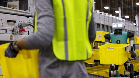Man with a blue robot both carrying a yellow tub 