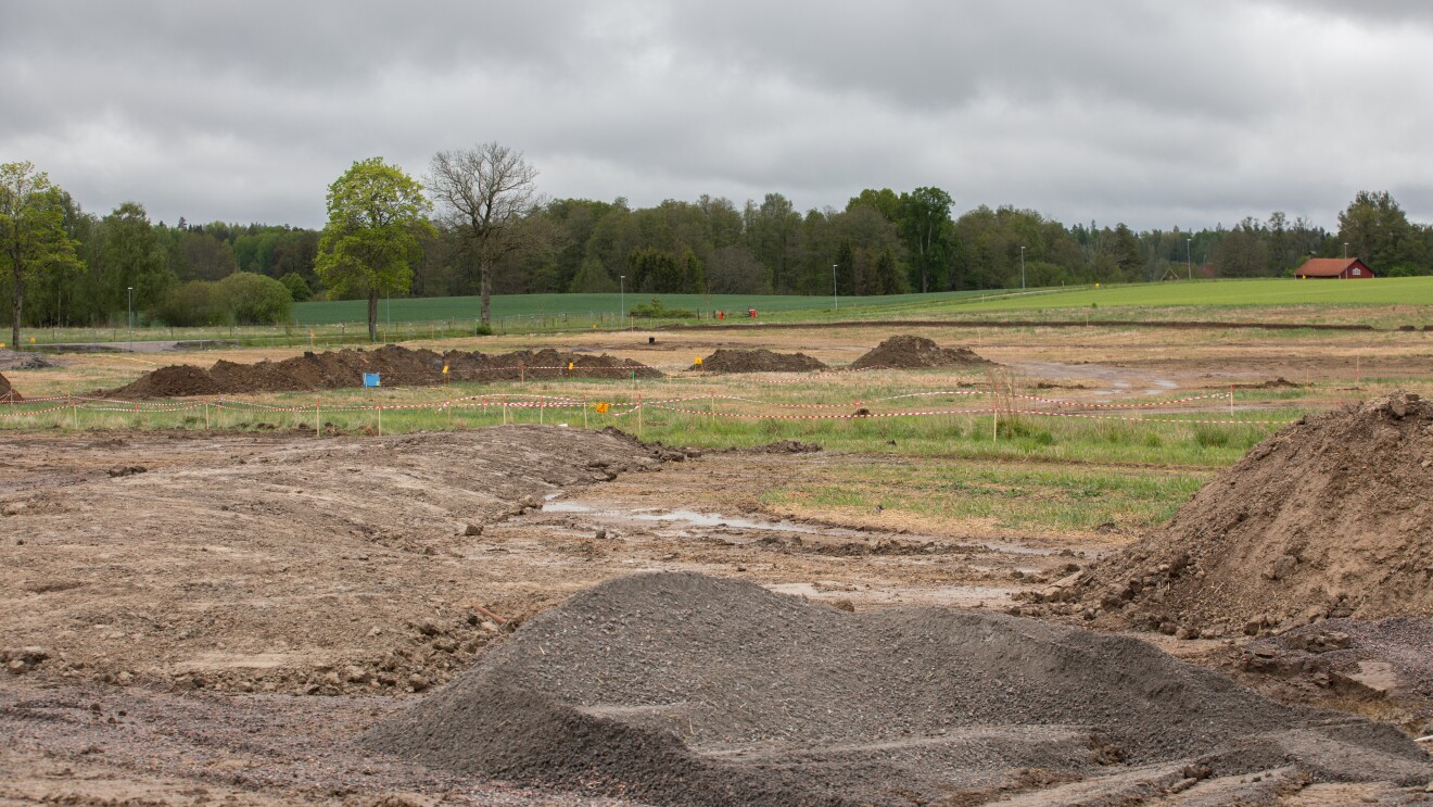 Excavation area surrounded by forest and fields under cloudy sky