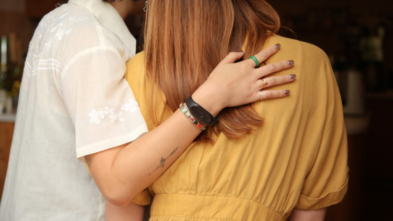 A person placing their hand on another person's back. The arm placed on the person's back is wearing a Bee device.