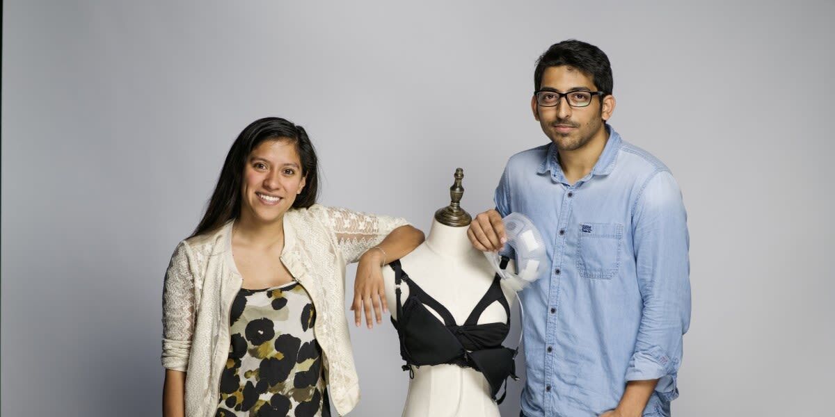 An image of a man and a woman smiling for a photo. Between them is a mannequin displaying a breastfeeding bra.  