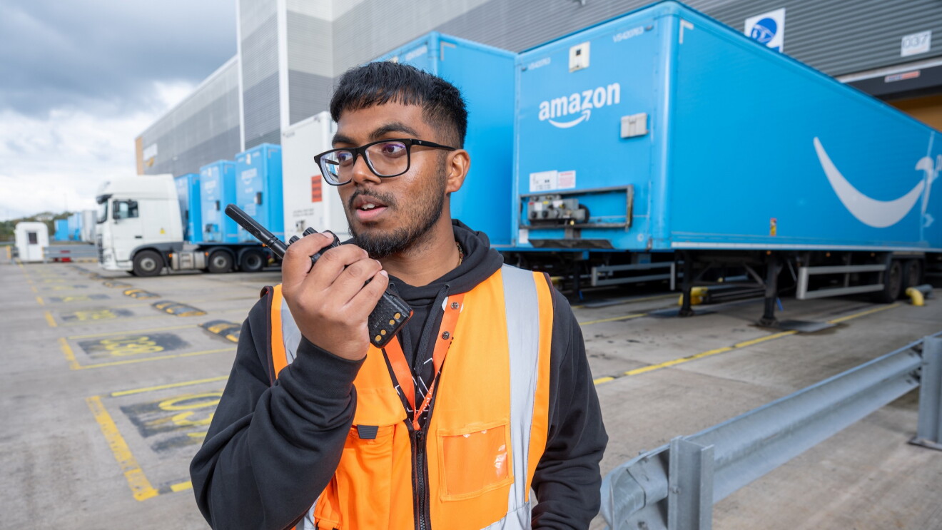 Young man stands outside a warehouse with a handheld transceiver