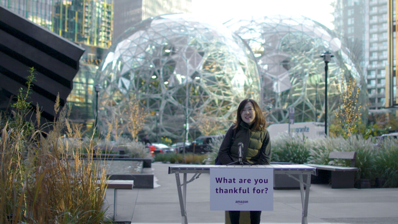 A woman sits at a table with a note that says "What are you thankful for?" - behind her are the Amazon Spheres. 