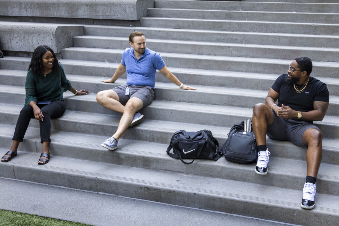 A woman and two men sit on a concrete staircase.