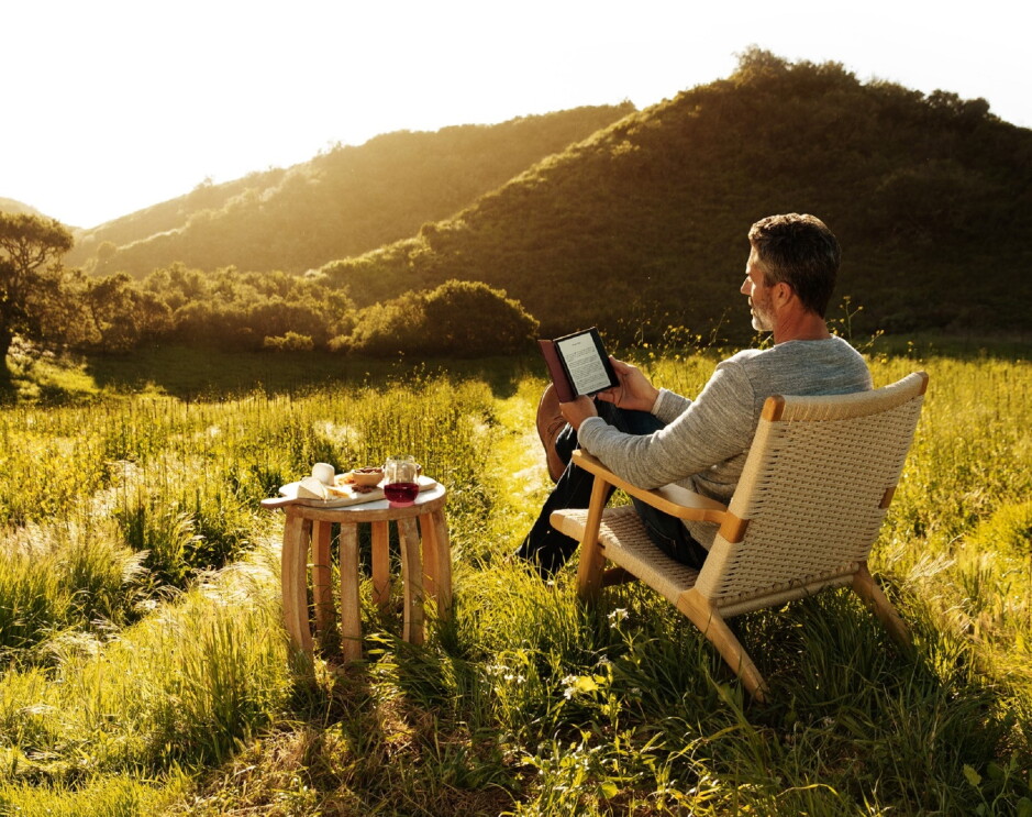 A man reading his all-new Kindle Oasis while looking out at the sun setting over a vineyard