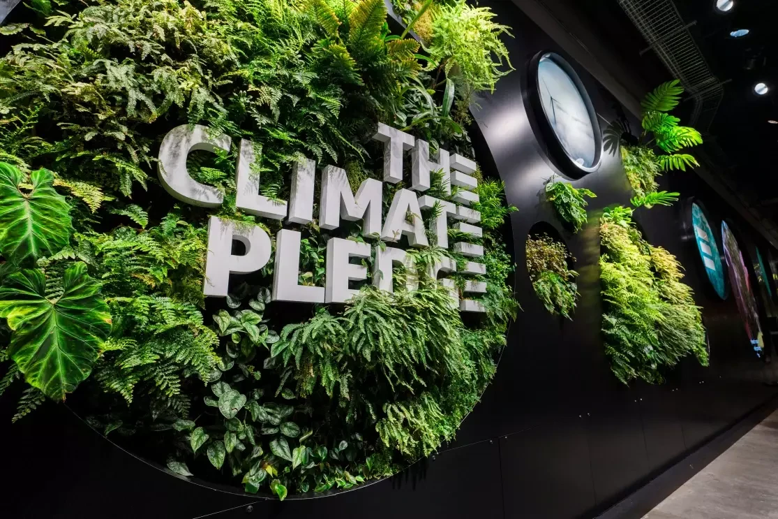 Dentro de una oficina de Amazon estáel cartel de The Cliamte Pledge dentro de un bosque vertical. 