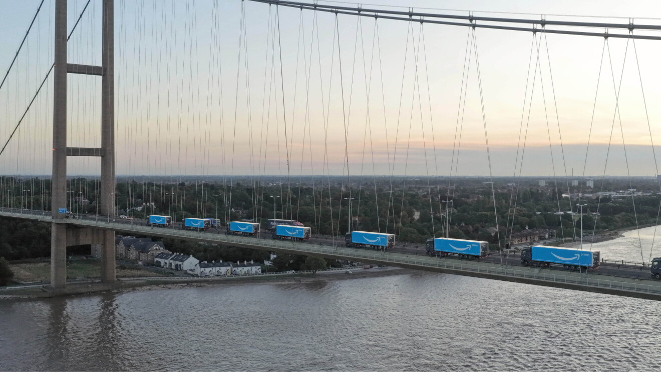 Amazon delivery trucks crossing suspension bridge over river at sunset
