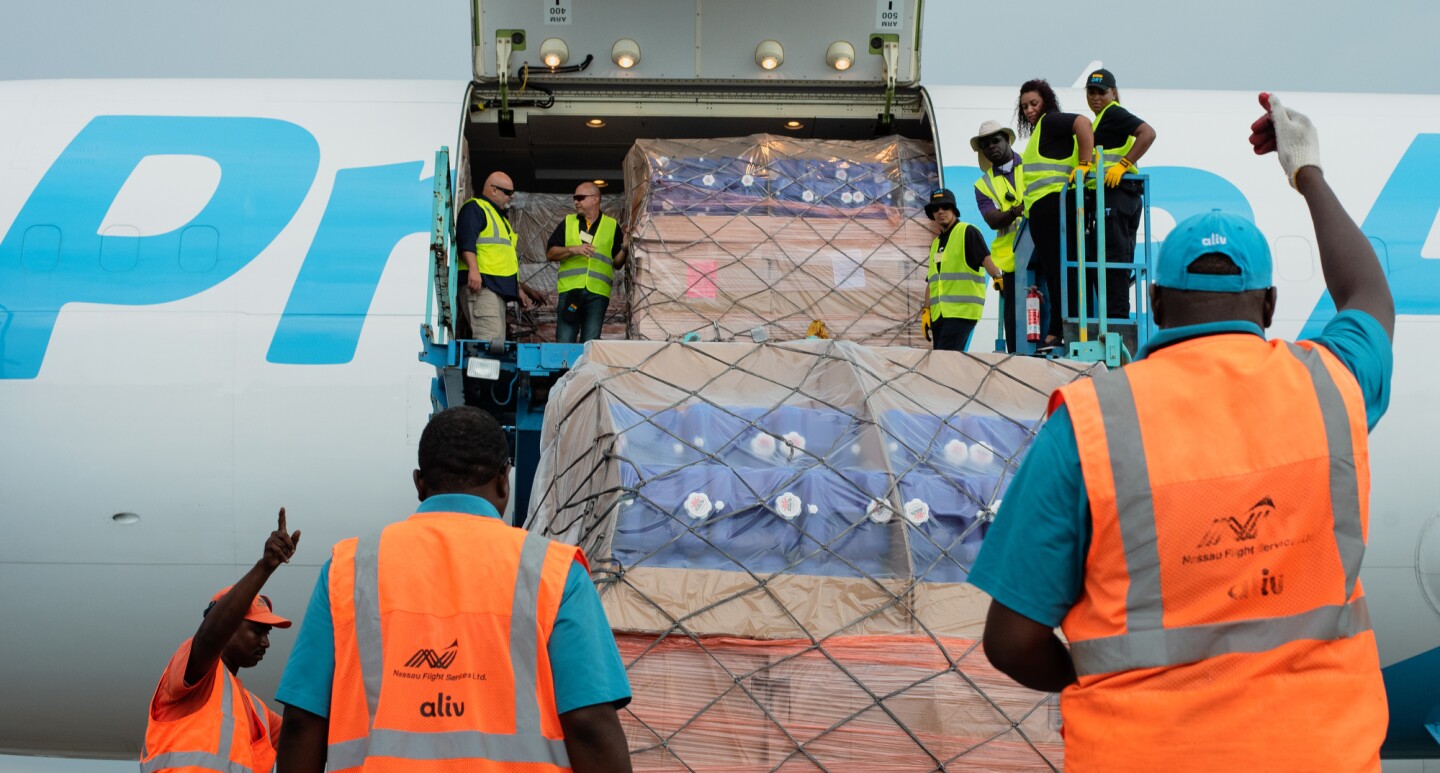 Employees in orange and yellow safety vests lift cargo supplies onto a Prime Air plane.