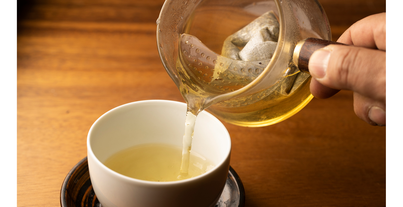 ガラスの急須から白い湯呑に黄金色のお茶が注がれる写真