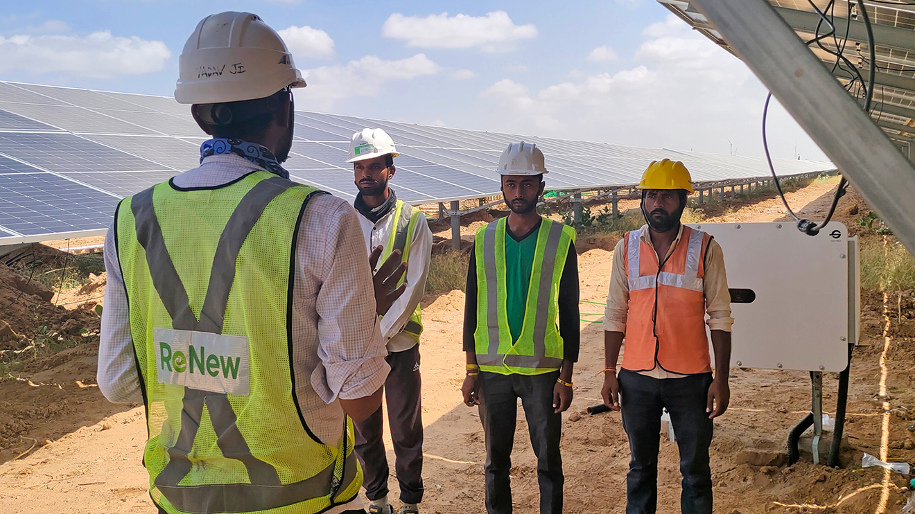 Uma foto de Awadhesh Kumar, engenheiro sênior da Amazon Solar Farm India—Rajasthan Jaisalmer, falando com sua equipe na fazenda solar. Há painéis solares ao fundo.