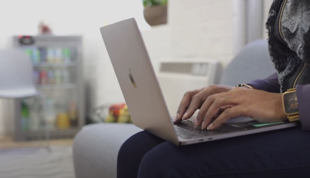 A woman types on the keyboard of a laptop computer while sitting on a sofa. 