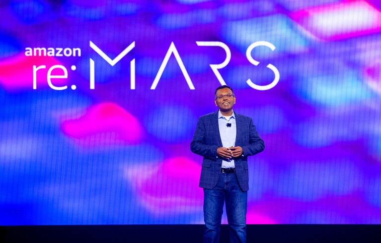 Swami Sivasubramanian smiling while standing on the keynote stage at re:MARS. Behind him is a colorful screen that says